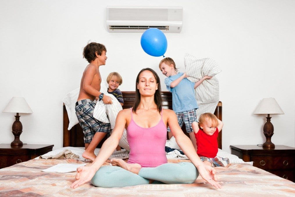 Woman in yoga pose with children playing behind her on bed