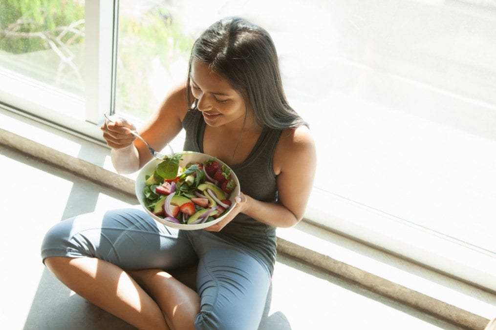 Pregnant woman eating bowl of fruits and vegetables
