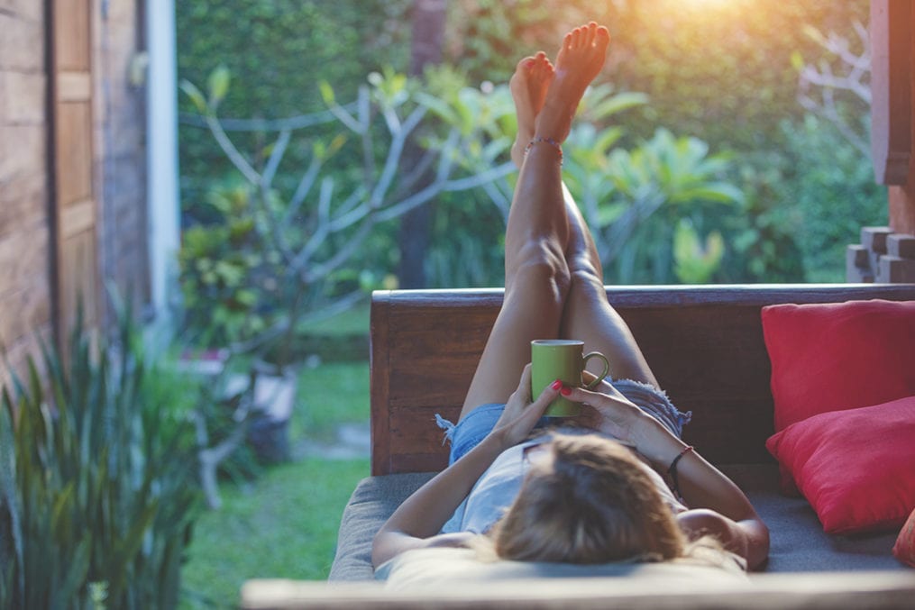 Girl enjoying early morning coffee on the garden sofa.