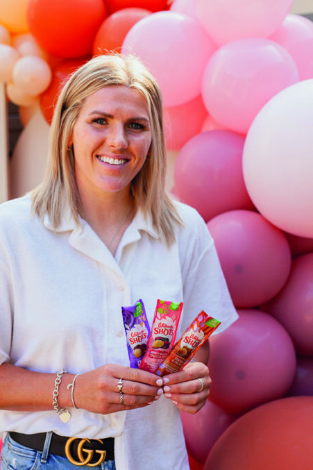 England and Chelsea footballer Millie Bright standing in front of a pile of balloons and holding some Whitworth Shots