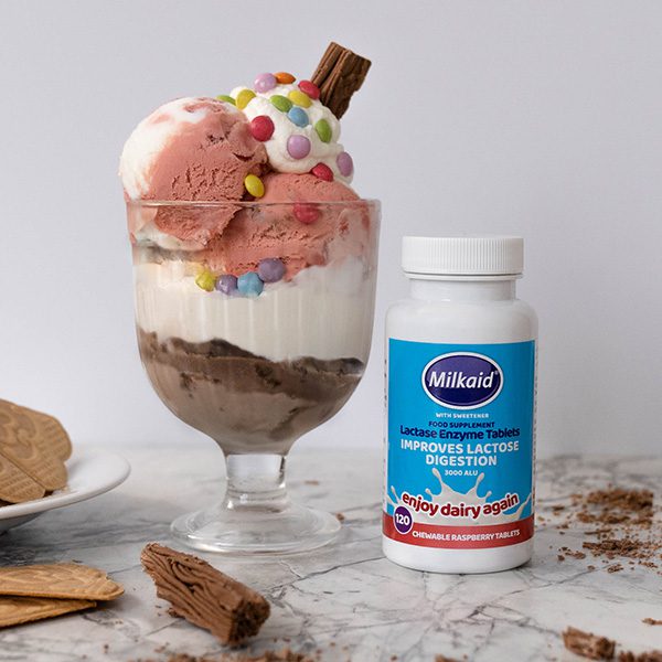 Ice cream sundae on a marble counter next to a jar of Milkaid lactase enzyme chewable tablets to treat lactose intolerance